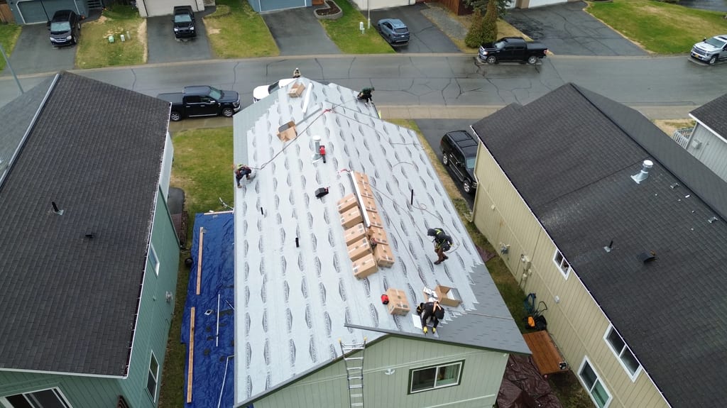 Aerial view of a suburban home with a partially installed metal roof, surrounded by lush greenery on a cloudy day.