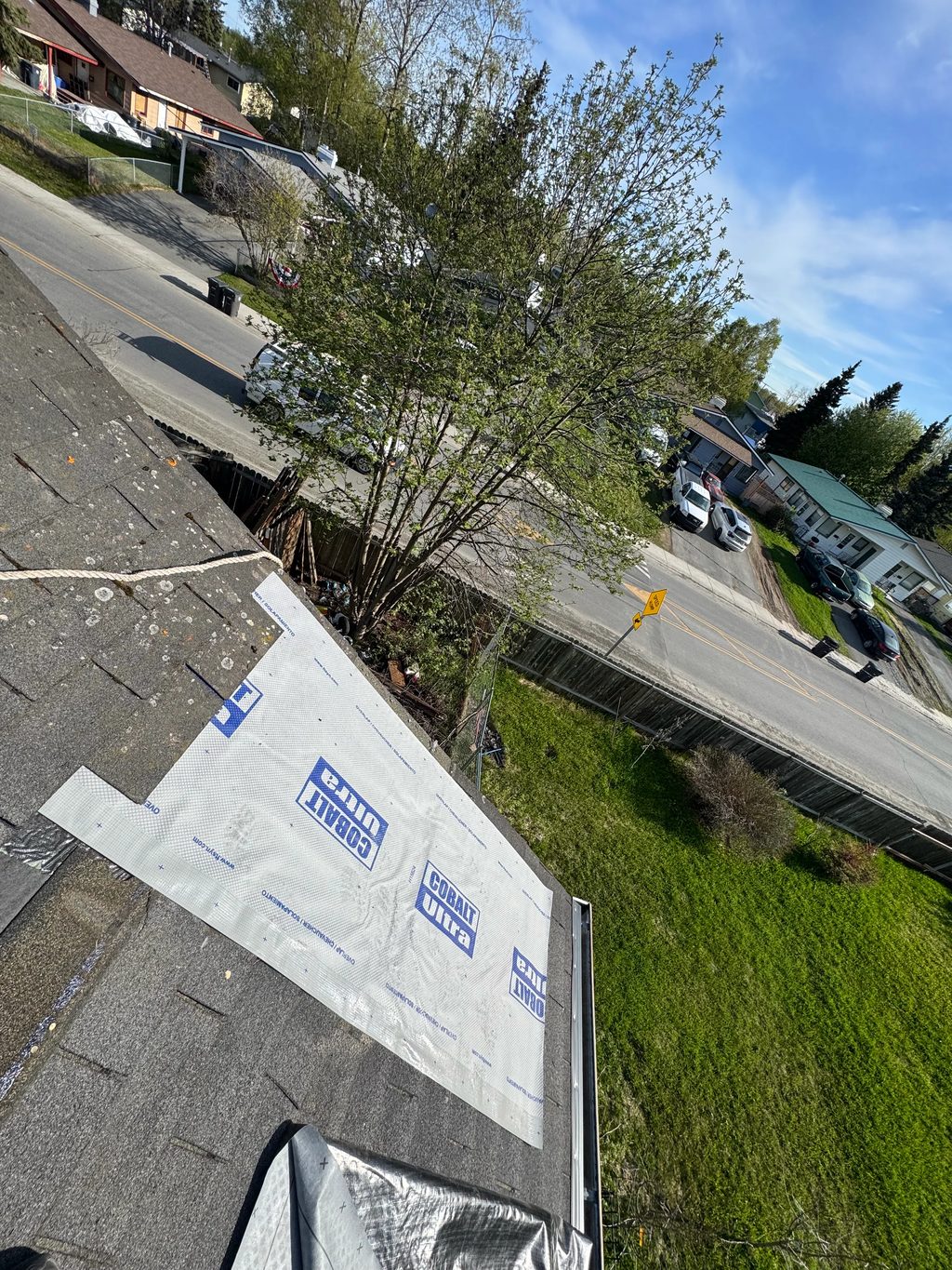 A modern single-family home with a metal roof under construction in a rural or suburban area with lush greenery and blue sky.