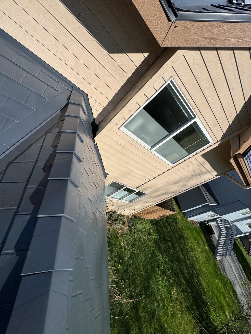 A modern-style single-family home with a metal roof and snow guards, situated in an urban or suburban area with lush greenery.