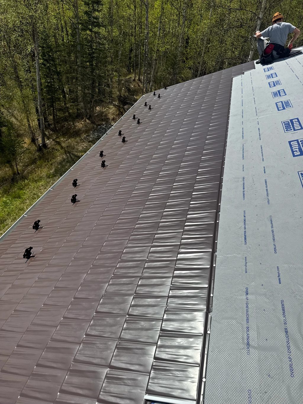 A metal roof under construction in a forested, rural area.