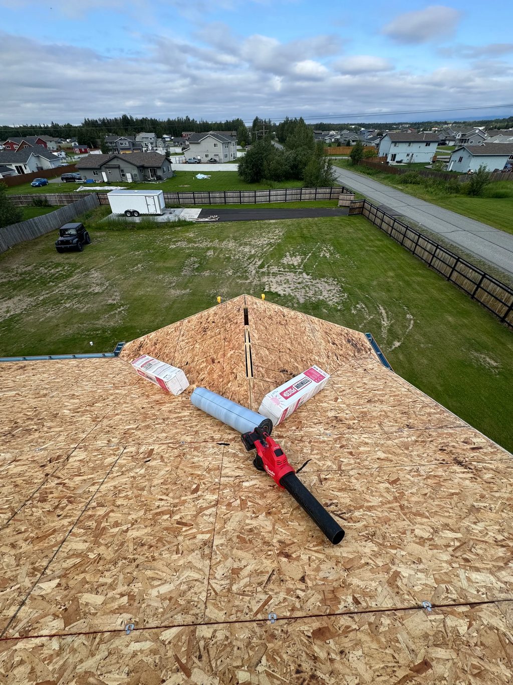 A metal roof in progress, with exposed decking and underlayment, on a suburban home with a brown roof