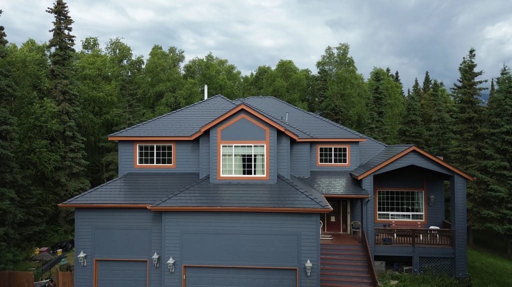 A large house with a grey roof and brown trim, set against a backdrop of trees.