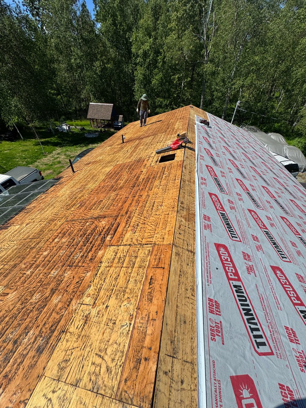 A metal roof is being installed on a house in a forested area.