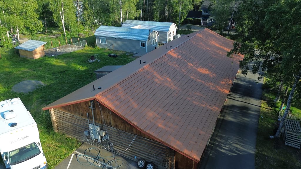 A large ranch-style home with a brown metal roof in a wooded area