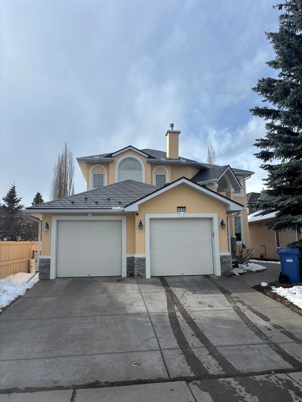 Weathered Interlock Slate aluminum roof on a yellow two-storey home with dormers among tall pines, Calgary, Alberta