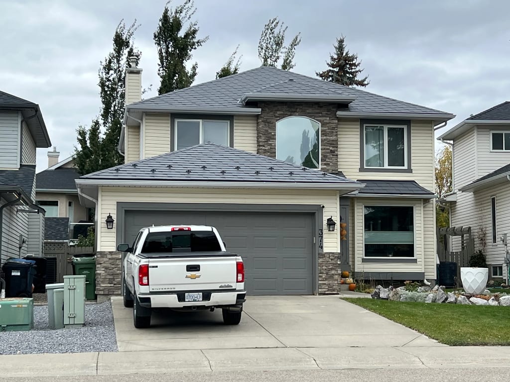 Charcoal Grey Interlock Slate aluminum roof on a two-storey home with dormers and stone accents among tall, Calgary, Alberta