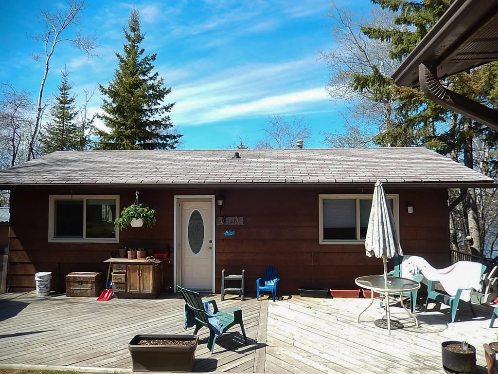 Tudor Brown Interlock Slate aluminum roof on a brown one-storey cottage with a grey roof among tall trees, Pelican Narrows, Alberta