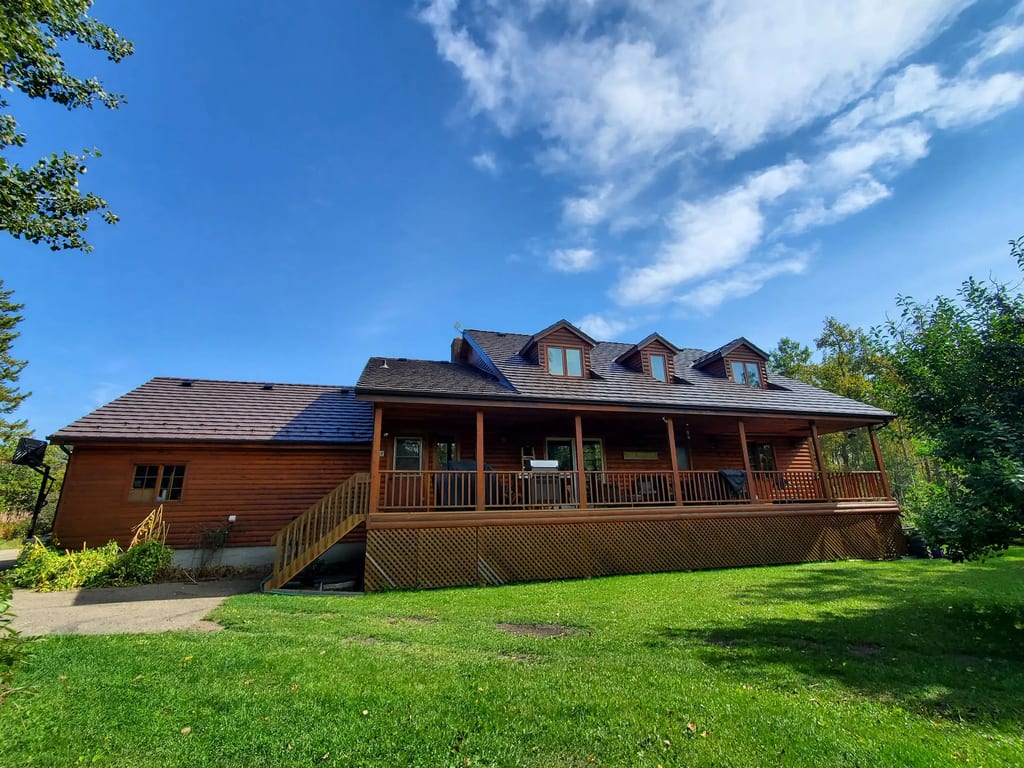 Large log-style farmhouse with Interlock Colonial Brown aluminum shake metal roof, three dormers, and wide wraparound deck in rural Red Deer County, AB.