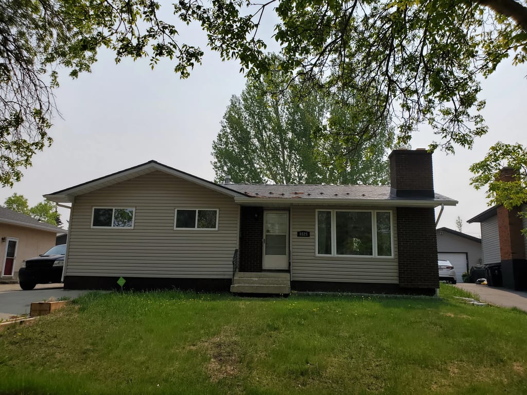 Black Interlock Slate aluminum roof on a brown single-storey home with a chimney among tall trees, Fort Saskatchewan, Alberta