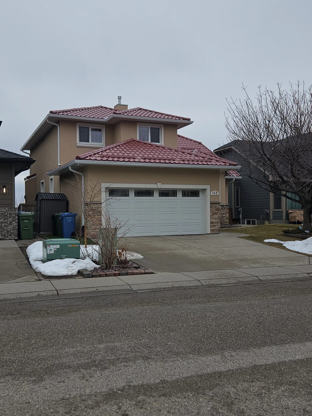 Tile Red Interlock Tile aluminum roof on a tan two-storey home with a red metal roof in an urban, Calgary, Alberta