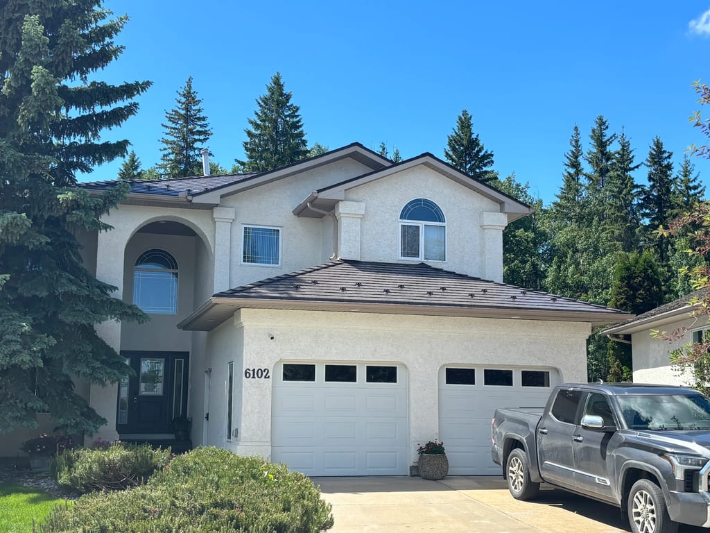 Tudor Brown Interlock Cedar Shingle aluminum roof on a white two-storey home with dormers among tall pines, Grande Prairie, Alberta