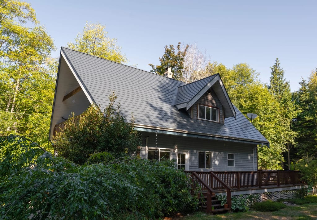 Deep Charcoal Interlock Cedar Shingle aluminum roof on a grey two-storey chalet with dormers among tall trees, Halfmoon Bay, British Columbia