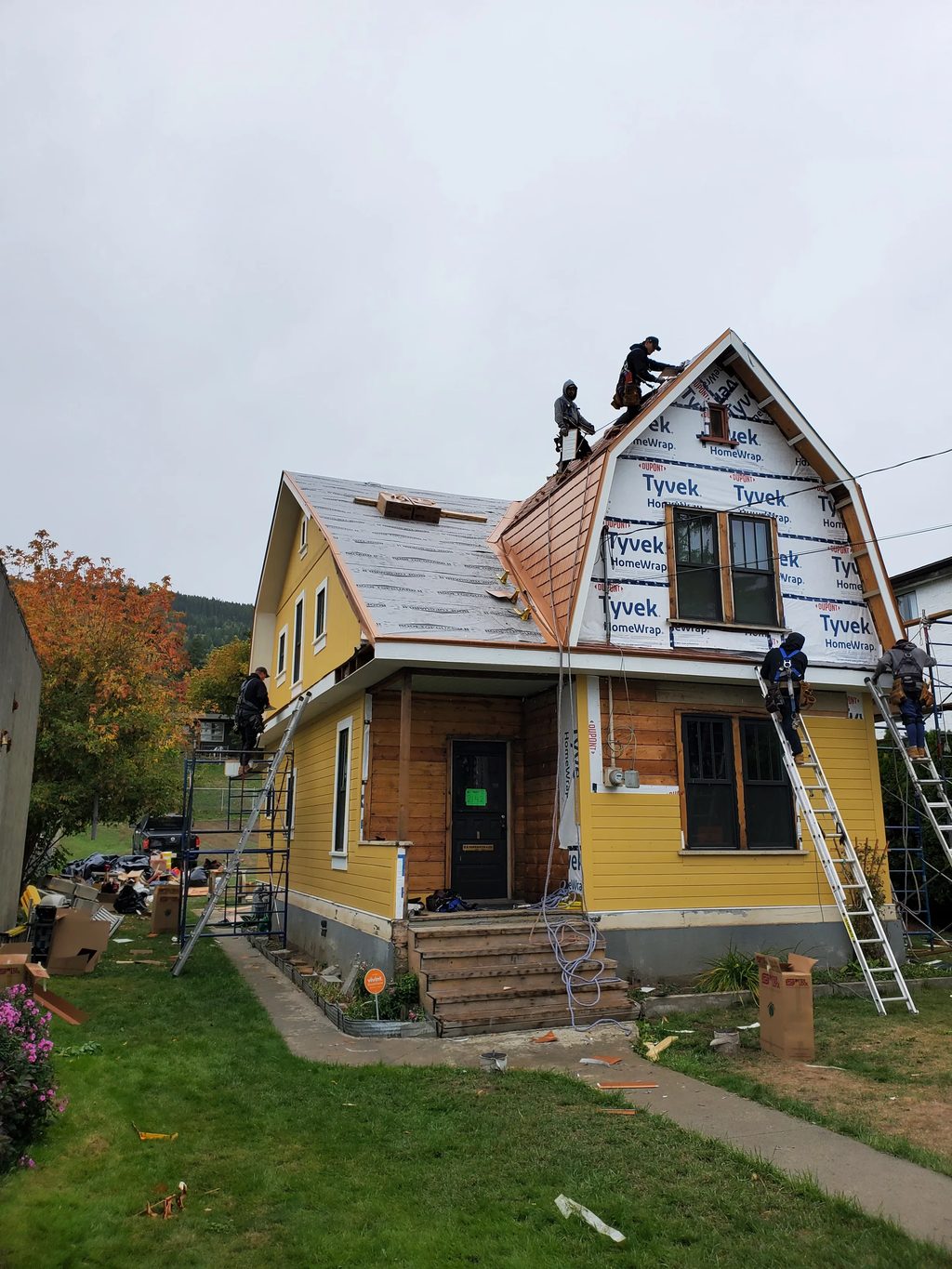 Copper Penny Interlock Cedar Shingle aluminum roof being installed on a yellow two-storey cottage with a metal roof under, Lumby, British Columbia