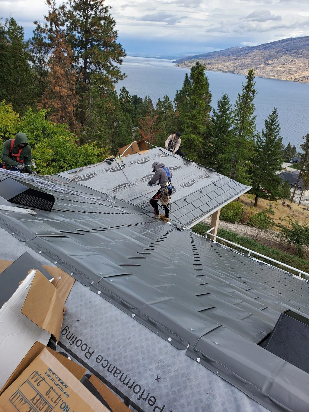 Musket Grey Interlock Slate aluminum roof being installed on a grey home with a metal roof under construction on a lake, Peachland, British Columbia