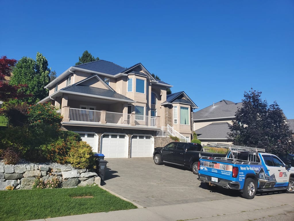 Deep Charcoal Interlock Slate aluminum roof on a tan two-storey home with a metal roof in a mountainous, Kelowna, British Columbia