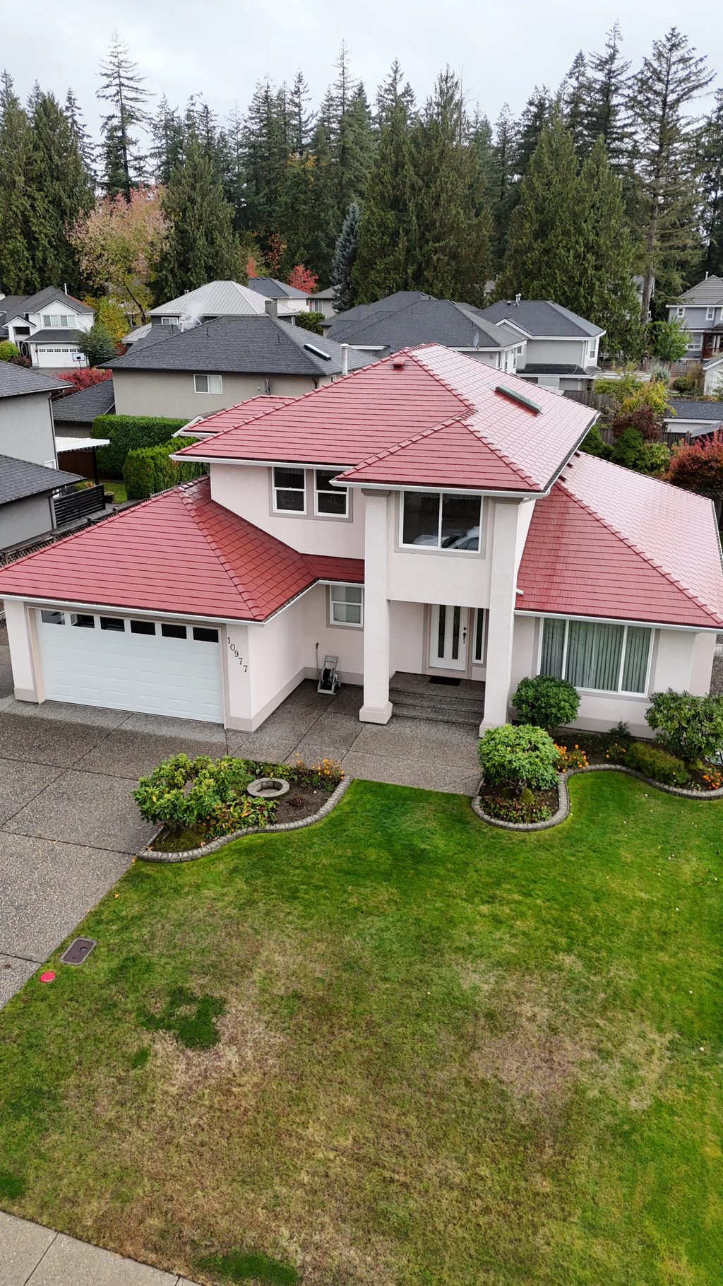 Tile Red Interlock Shingle aluminum roof on a red two-storey home with dormers among tall trees, Surrey, British Columbia