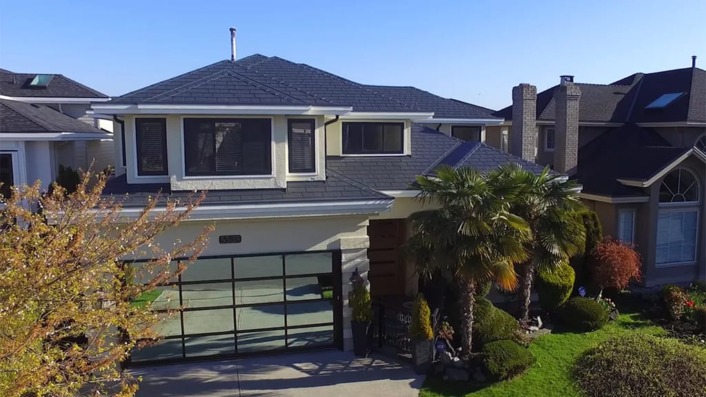 Deep Charcoal Interlock Slate aluminum roof on a two-storey home with a metal roof among trees and houses, Richmond, British Columbia