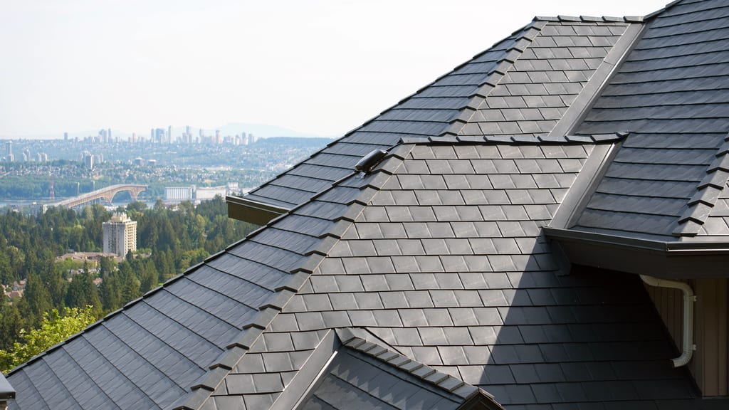 Close-up of a multi-hip deep charcoal Interlock aluminum slate metal roof with complex valleys and ridge caps, overlooking the North Vancouver skyline.