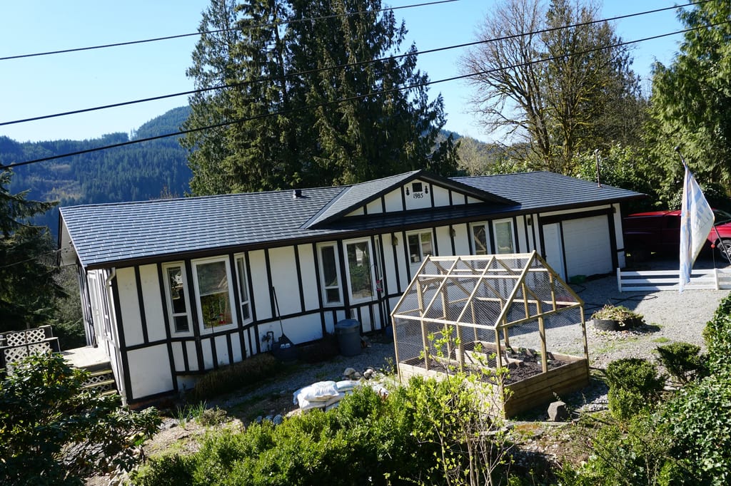 Deep Charcoal Interlock Slate aluminum roof on a white ranch-style home with a metal roof amidst evergreen, Mission, British Columbia