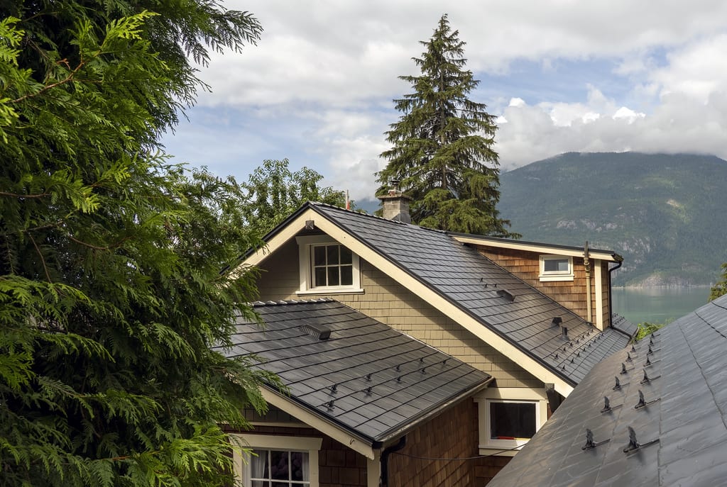 Black Interlock aluminum slate metal roof with multiple dormers and snow guards on a Craftsman home with mountain and water backdrop in Britannia Beach, BC.