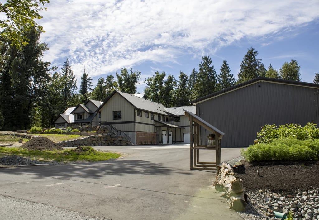 Musket Grey Interlock Slate aluminum roof on a two-storey home with dormers among tall conifers, Abbotsford, British Columbia