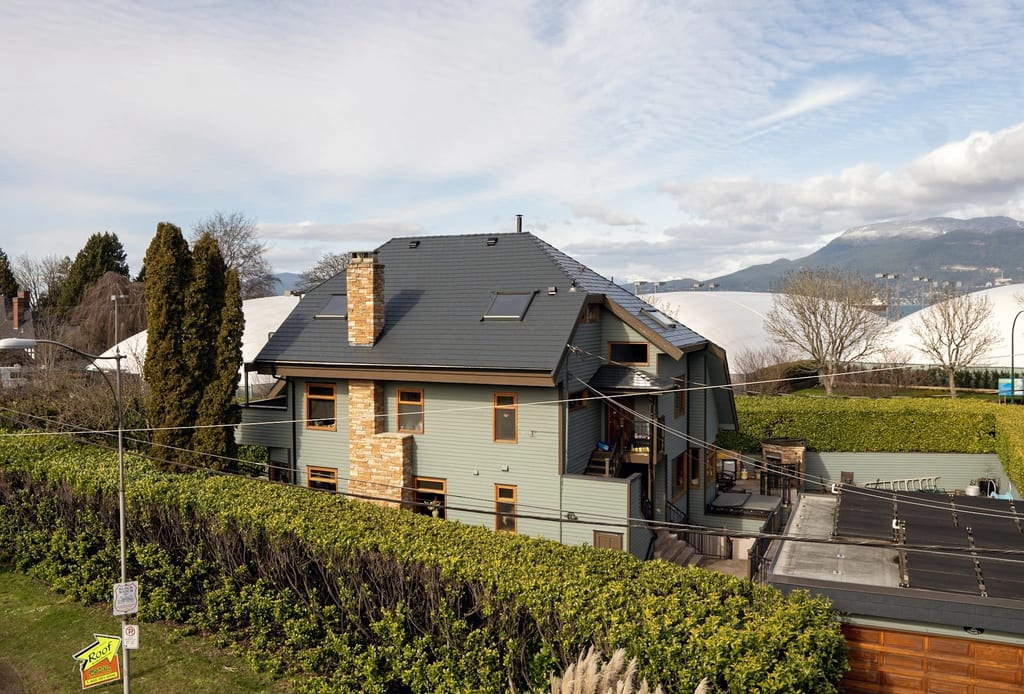 Rear elevation of a Craftsman home in West Point Grey, BC, featuring a complex deep charcoal aluminum slate metal roof with skylights and stone chimney.