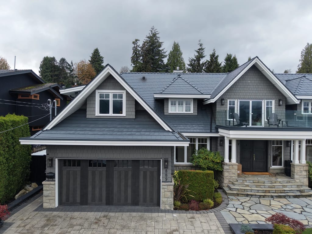 Deep Charcoal Interlock Slate aluminum roof on a grey two-storey home with dormers among tall pines, North Vancouver, British Columbia