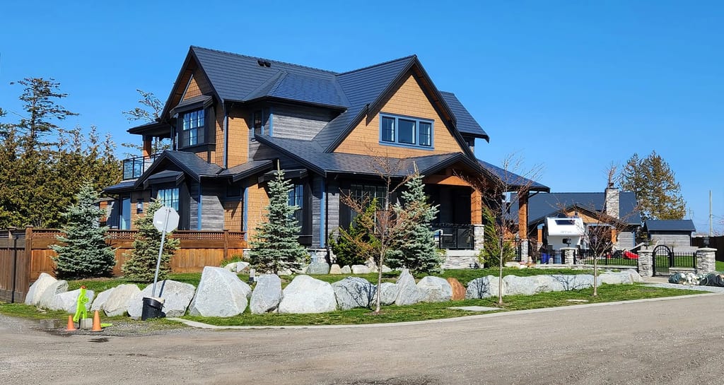 Two-storey Craftsman home in Tsawwassen BC with a complex steep Interlock aluminum slate roof in deep charcoal, boulder-lined landscaping, and cedar accents.