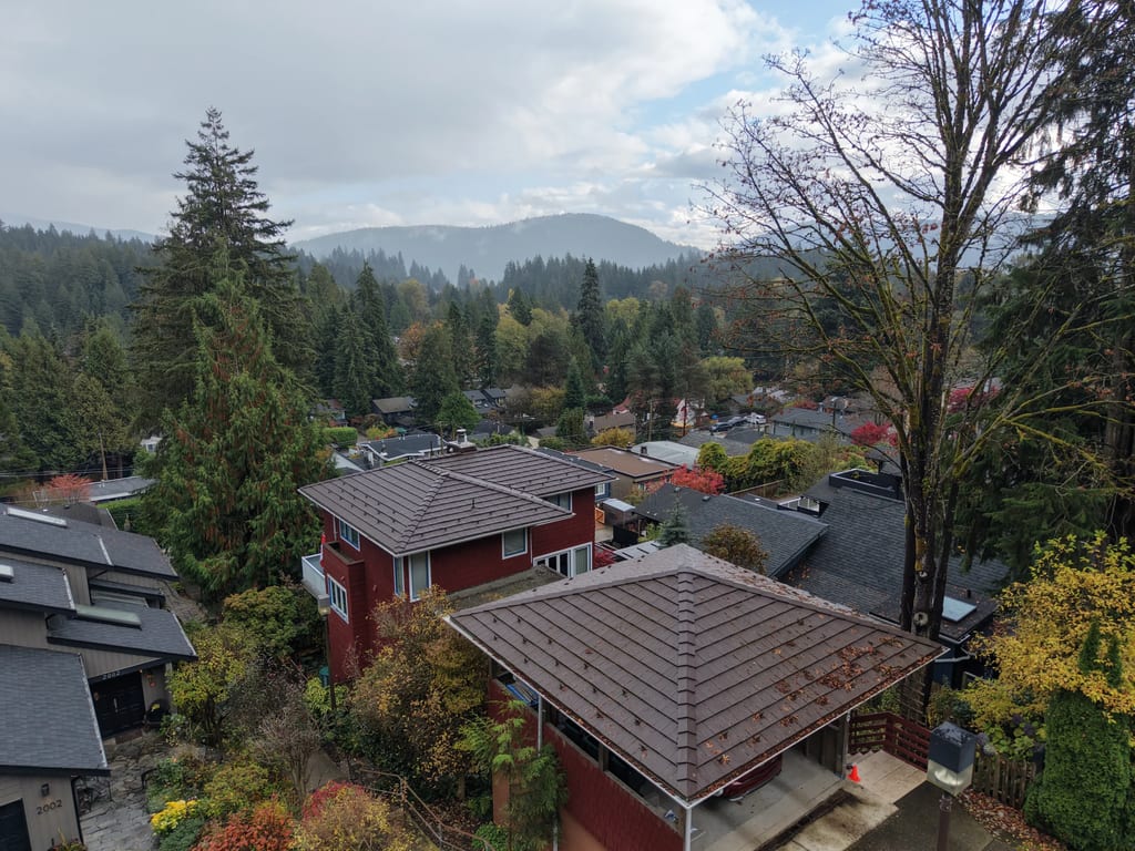 Colonial Brown Interlock Shake aluminum roof on a red two-storey home with a brown metal roof among tall, North Vancouver, British Columbia