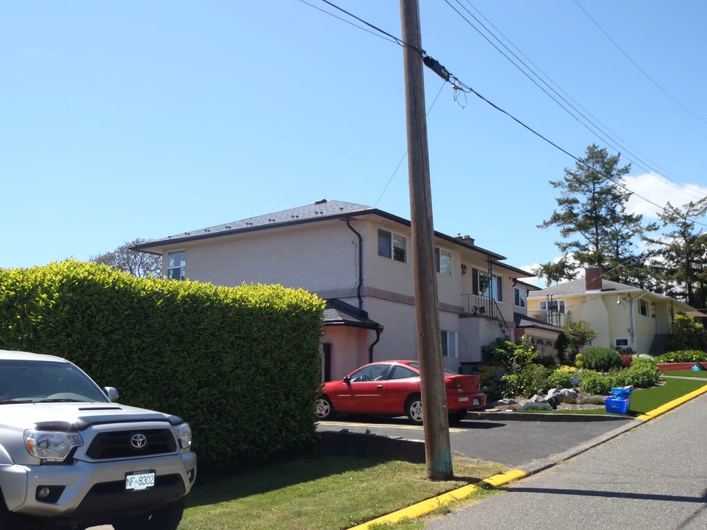 Black Interlock Slate aluminum roof on a beige two-storey home with a metal roof under, Victoria, British Columbia