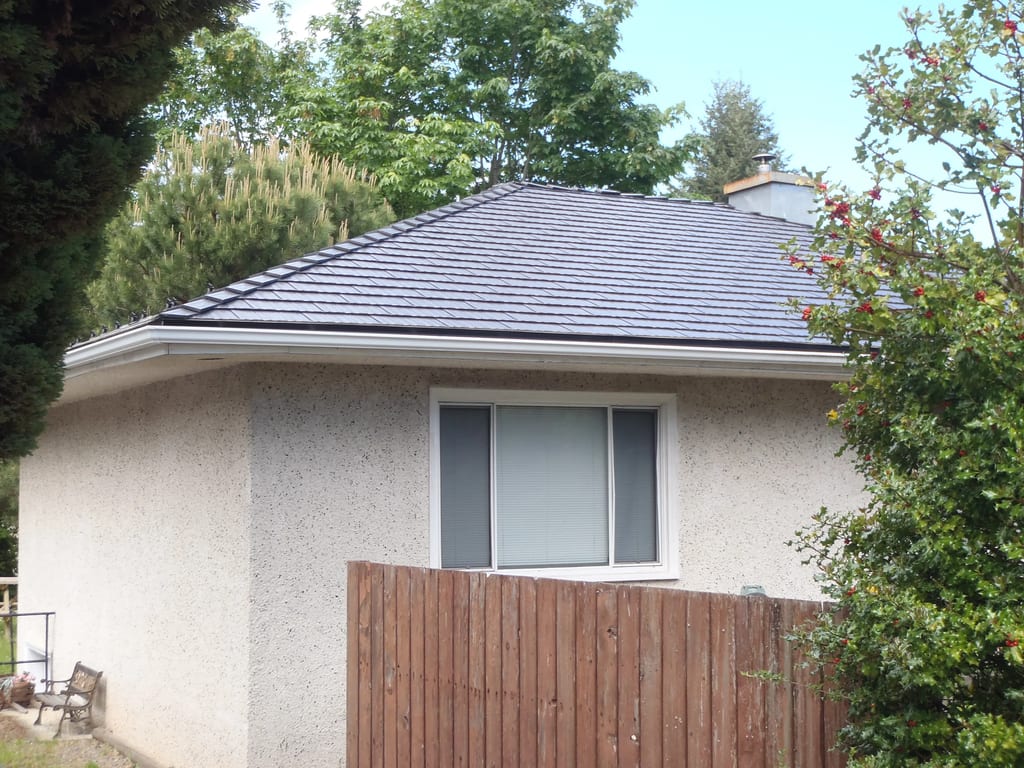 Black Interlock Cedar Shingle aluminum roof on a white home with a metal roof among tall green trees, Chemainus, British Columbia