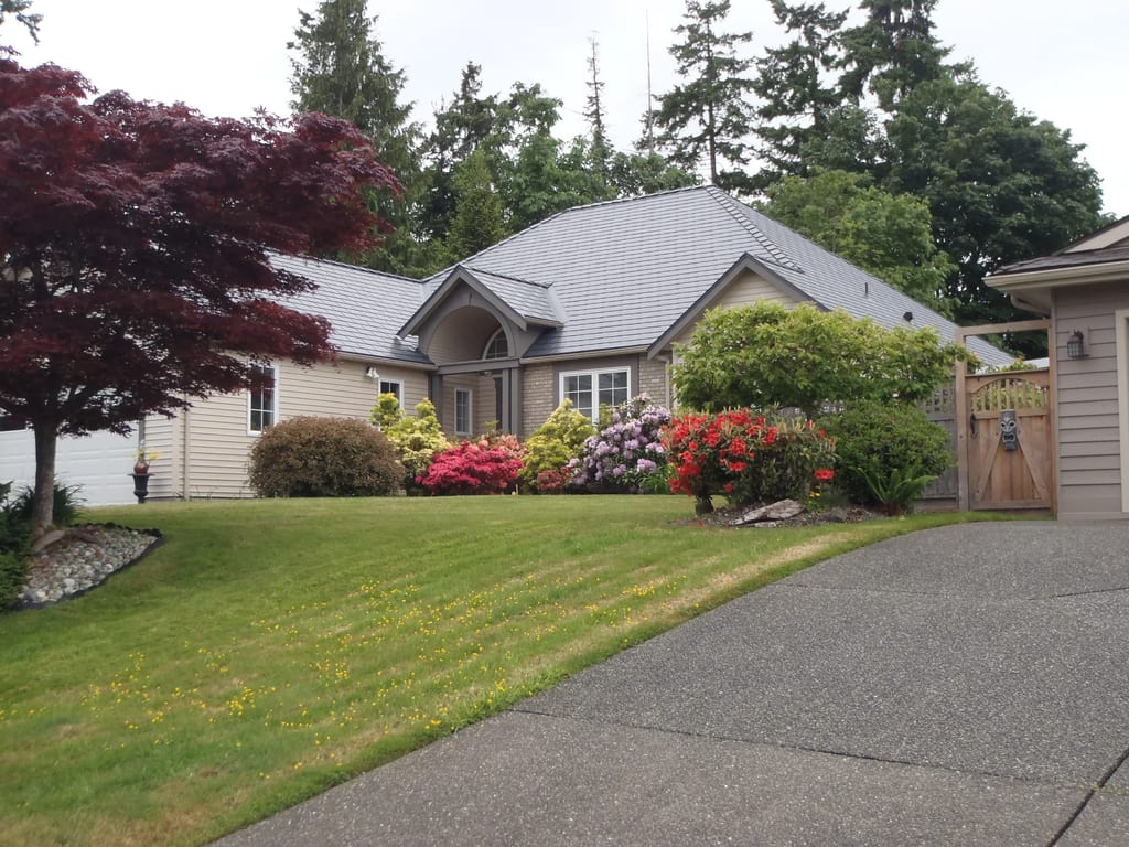 Deep Charcoal Interlock Slate aluminum roof on a beige home with a grey roof among tall trees, Qualicum Beach, British Columbia