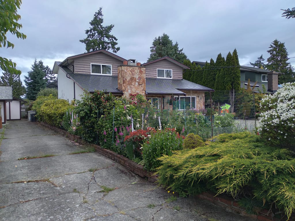 Black Interlock Slate aluminum roof on a two-storey home with a metal roof among trees and shrubs, Victoria, British Columbia