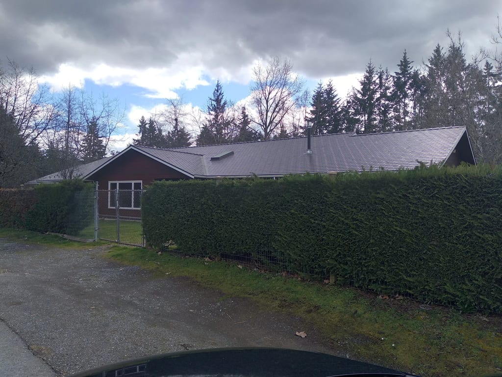 Tudor Brown Interlock Slate aluminum roof on a Tudor brown single-storey home among tall evergreens, Duncan, British Columbia