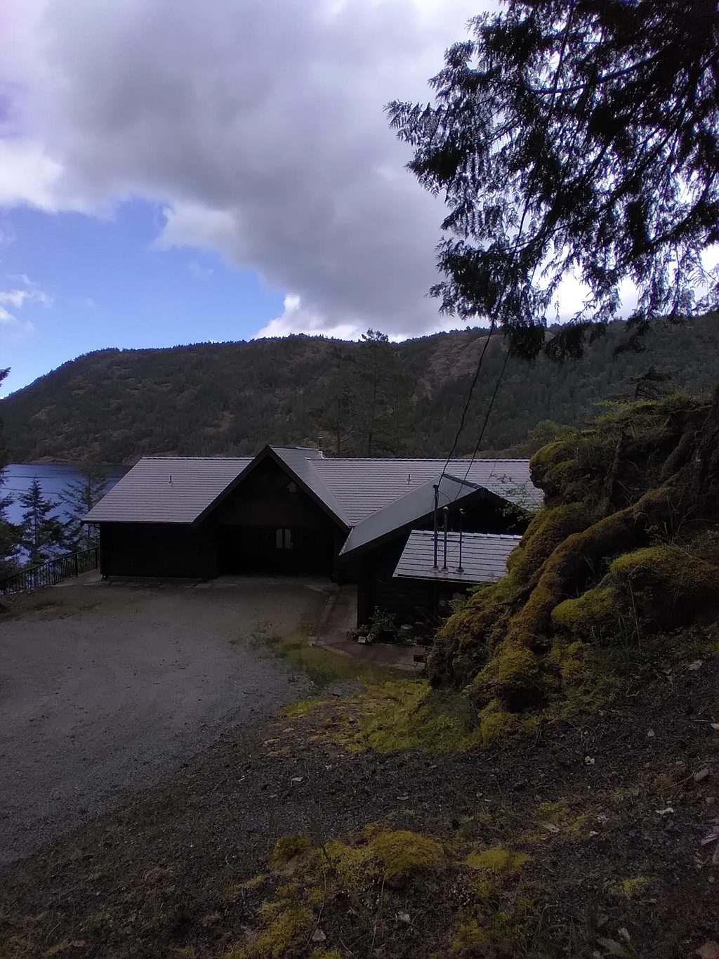 Deep Charcoal Interlock Slate aluminum roof being installed on a dark home with a metal roof among trees and a lake, Juan de Fuca, British Columbia