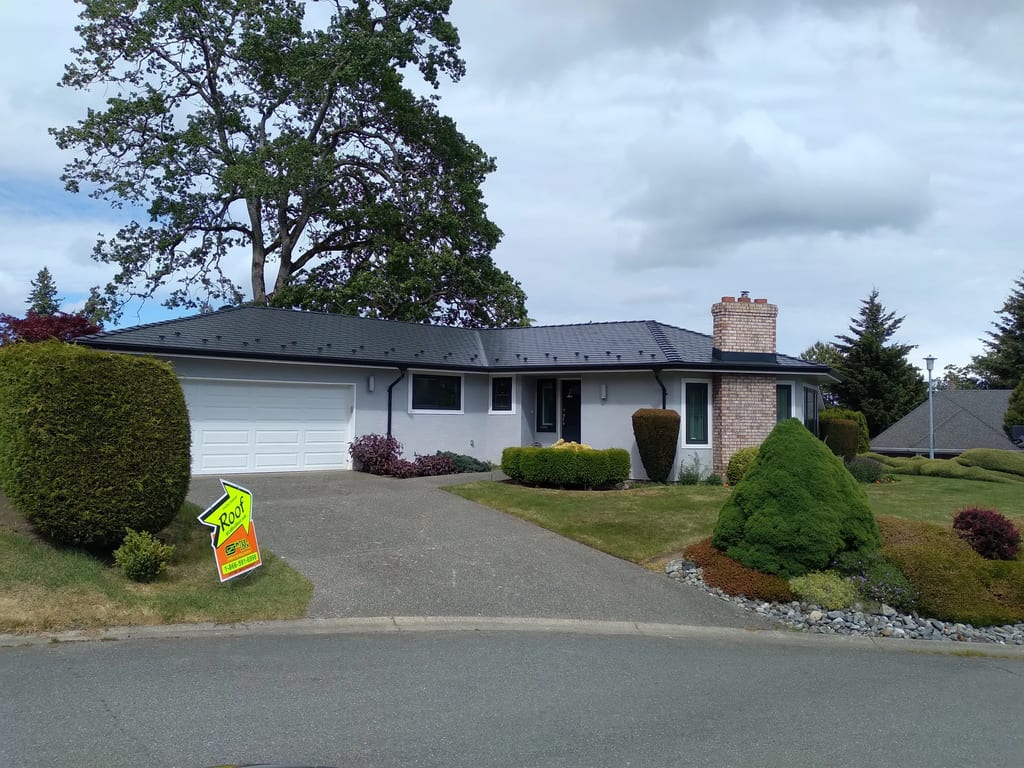 Black Interlock Slate aluminum roof on a white ranch home with a chimney among tall trees, Victoria, British Columbia