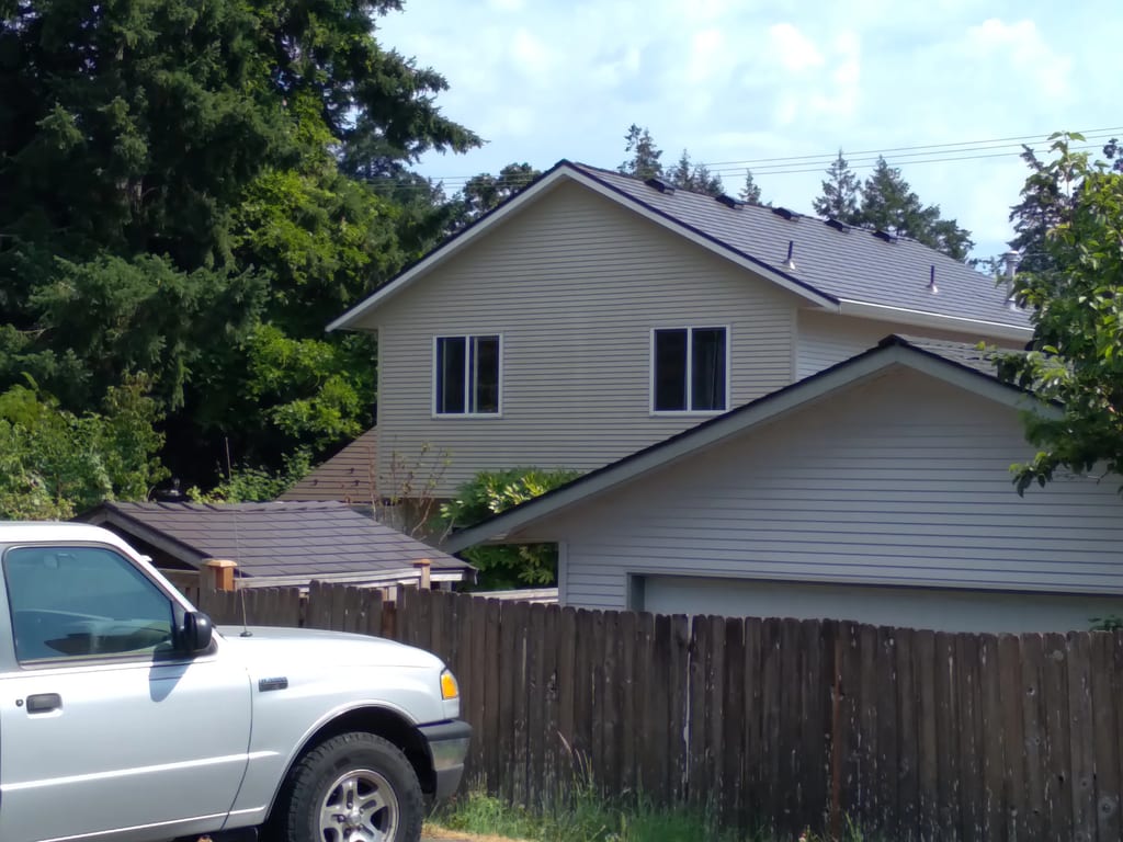 Tudor Brown Interlock Cedar Shingle aluminum roof on a Tudor two-storey home with dormers among tall trees, Victoria, British Columbia