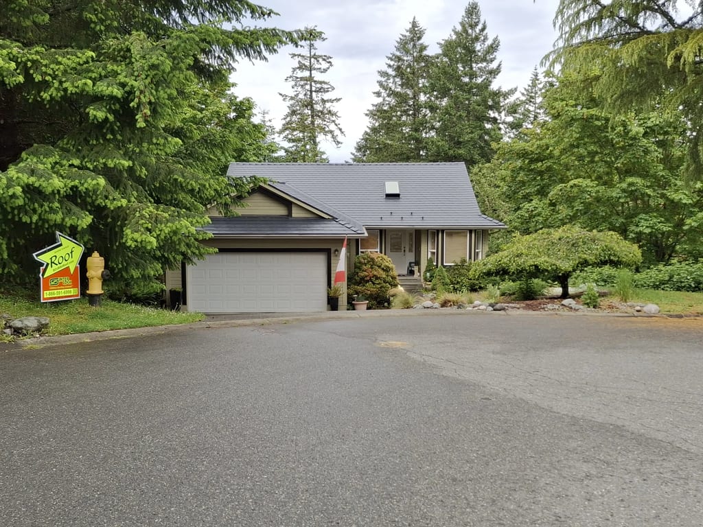 Black Interlock Slate aluminum roof on a beige home with a garage and dormers in a wooded setting, Duncan, British Columbia