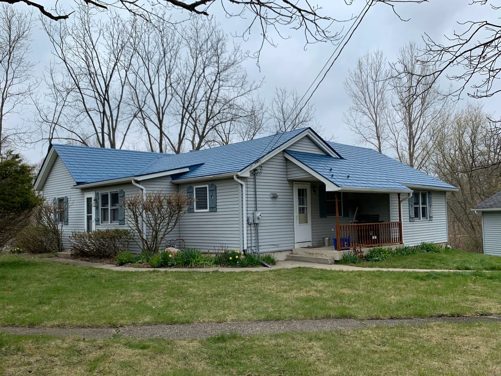 Royal Blue Interlock Slate aluminum roof on a grey ranch home with a metal roof and porch among tall, Woodstock, Illinois