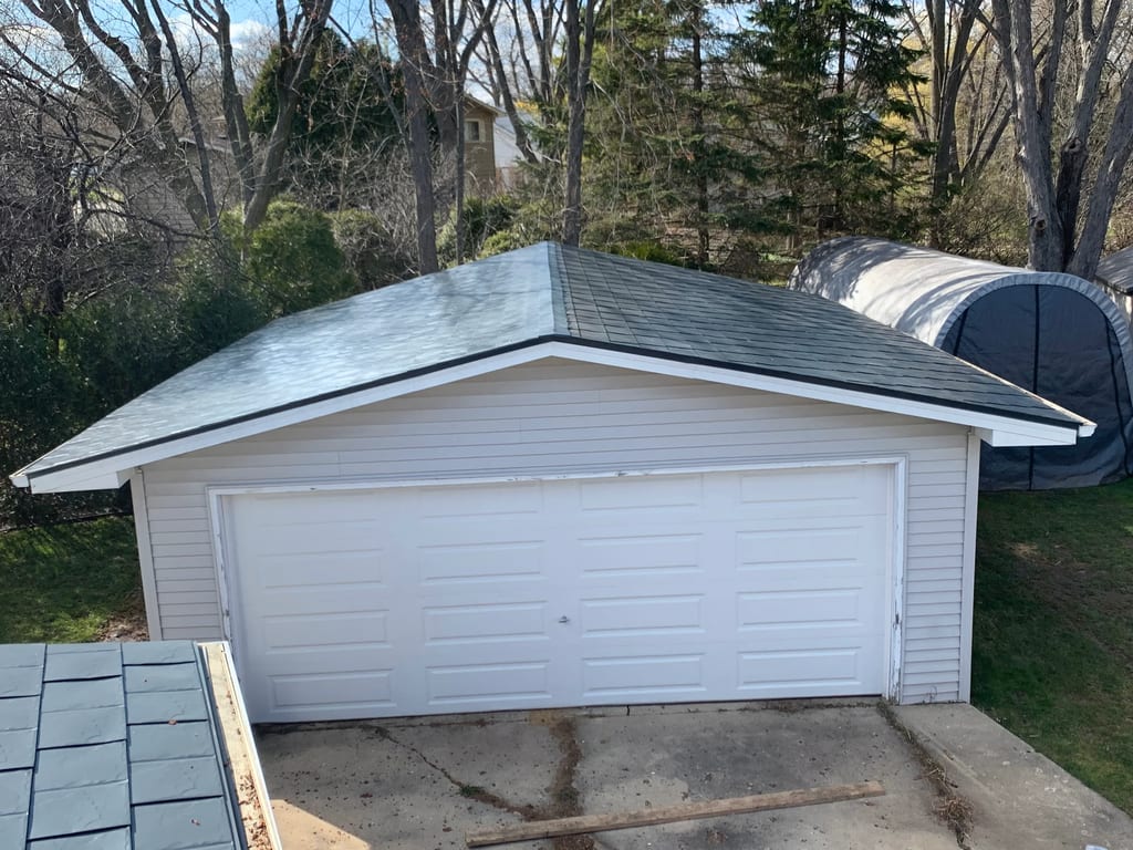 Deep Charcoal Interlock Slate aluminum roof on a white one-storey home with a garage among tall evergreens, Waukegan, Illinois