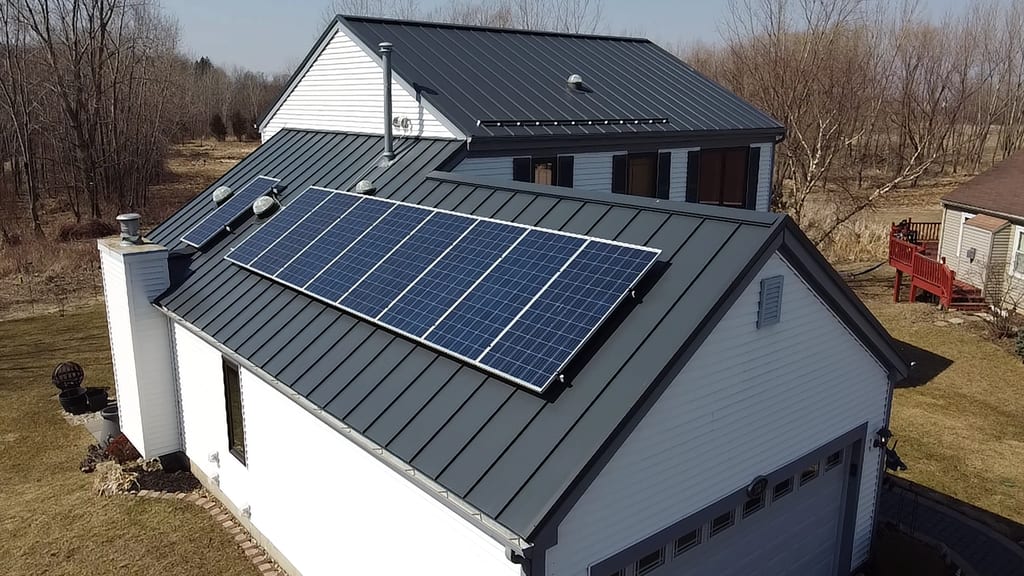 Aerial front view of a farmhouse with Deep Charcoal Interlock standing seam metal roof featuring a large solar panel array and front dormer.