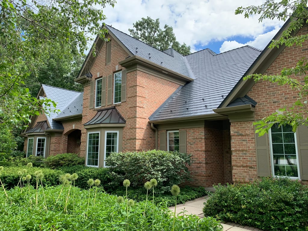 Deep Charcoal Interlock Slate aluminum roof on a brick home with a metal roof among tall trees, Crystal Lake, Illinois