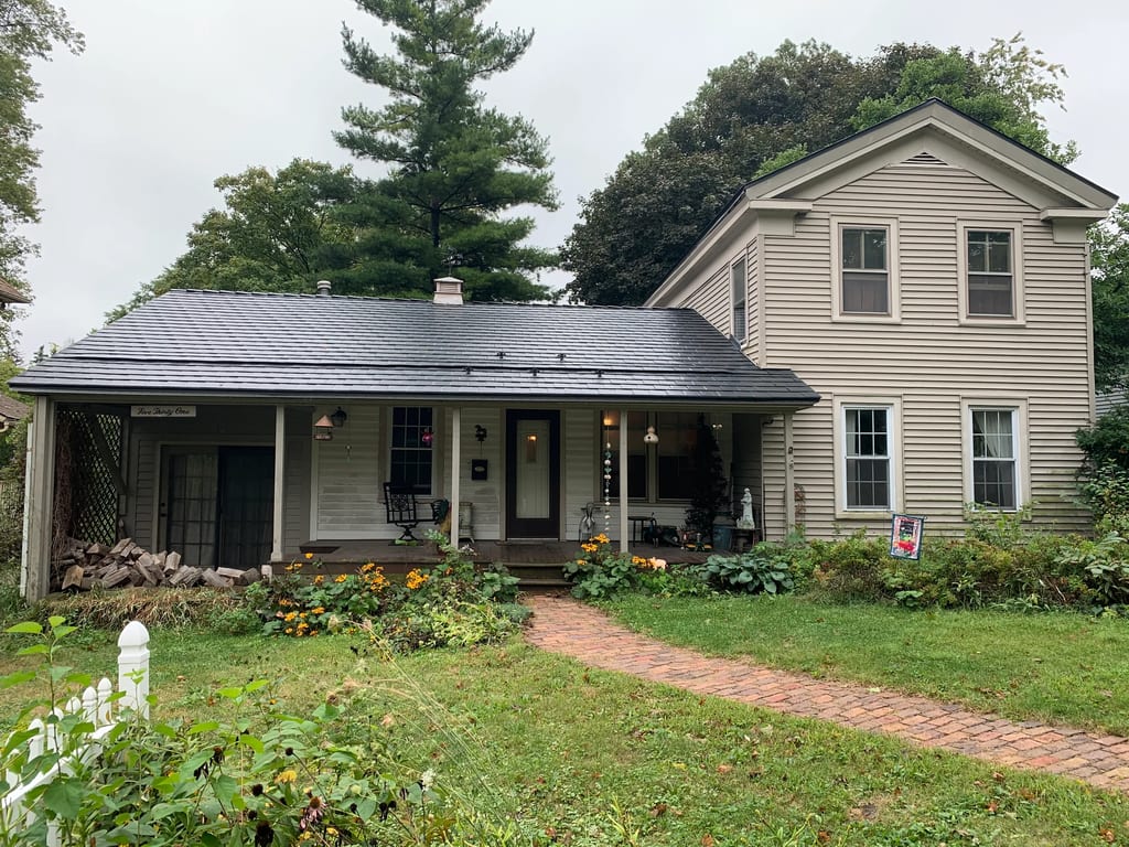 Black Interlock Slate aluminum roof on a tan two-storey farmhouse with a covered front porch among, Woodstock, Illinois
