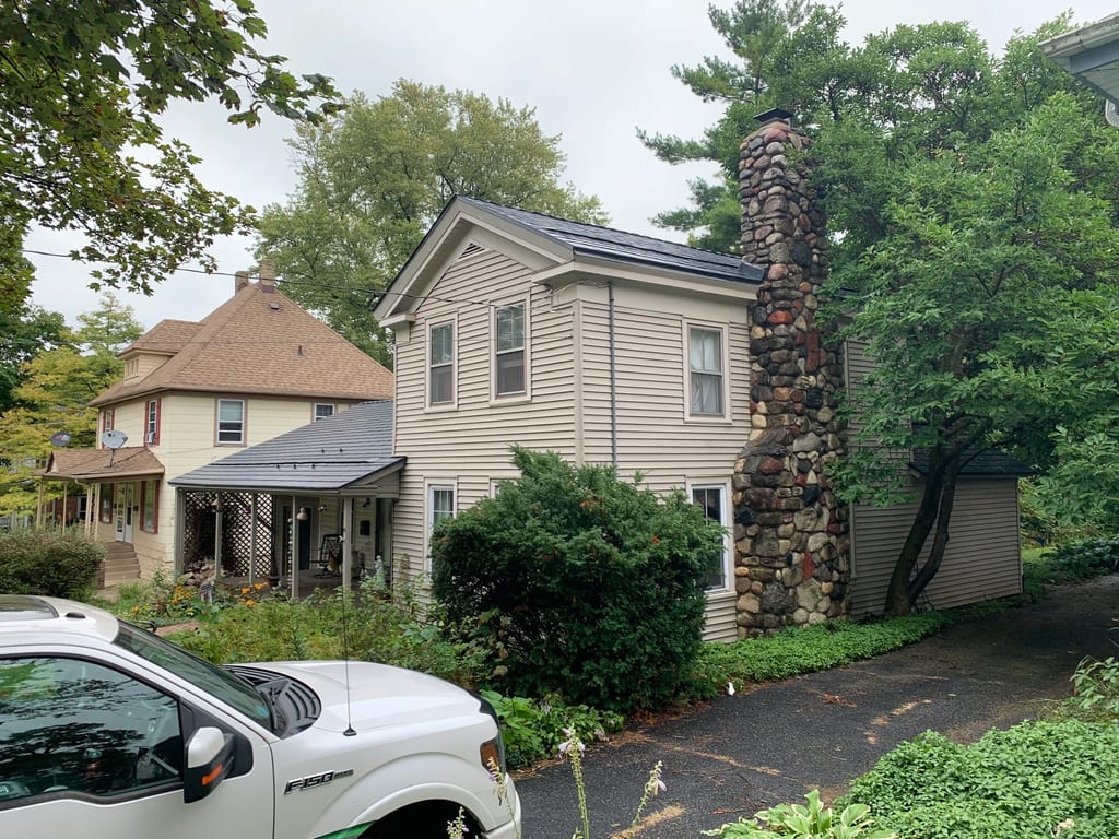 Black Interlock Slate aluminum roof on a beige two-storey colonial home among trees in a suburban, Woodstock, Illinois