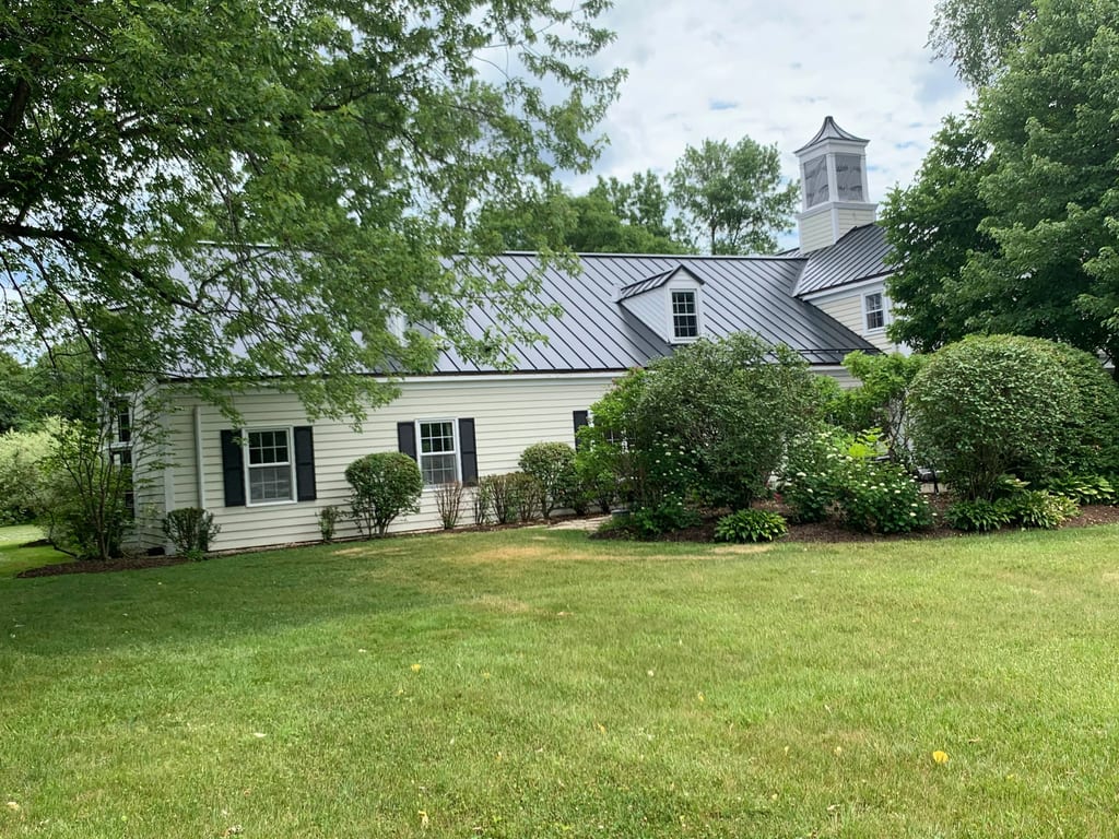 Black Interlock Standing Seam aluminum roof on a white Colonial home with dormers on a forested lakeside, Lake Forest, Illinois