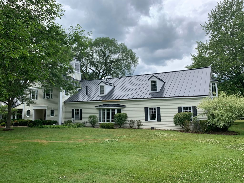 Black Interlock Standing Seam aluminum roof on a white colonial home with dormers among tall trees, Lake Forest, Illinois