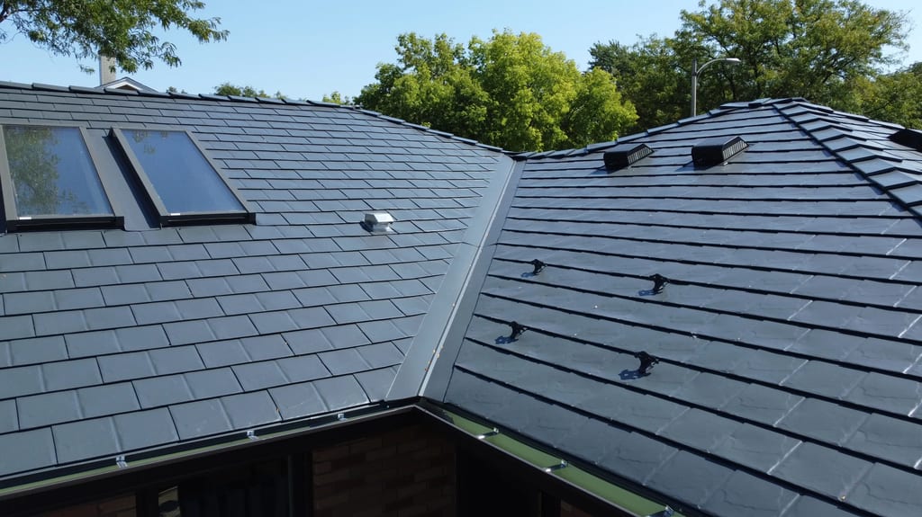 Deep Charcoal Interlock Slate aluminum roof on a dark two-storey home with a metal roof among tall trees, Westmont, Illinois