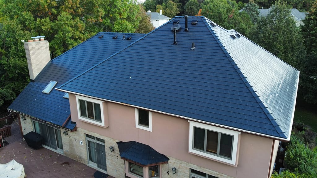 Black Interlock Slate aluminum roof on a tan house with a dark blue metal roof among trees, Lemont, Illinois