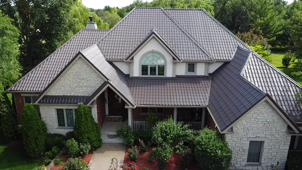 Tudor Brown Interlock Tile aluminum roof on a white single-family Tudor home in a forested suburban, Lemont, Illinois
