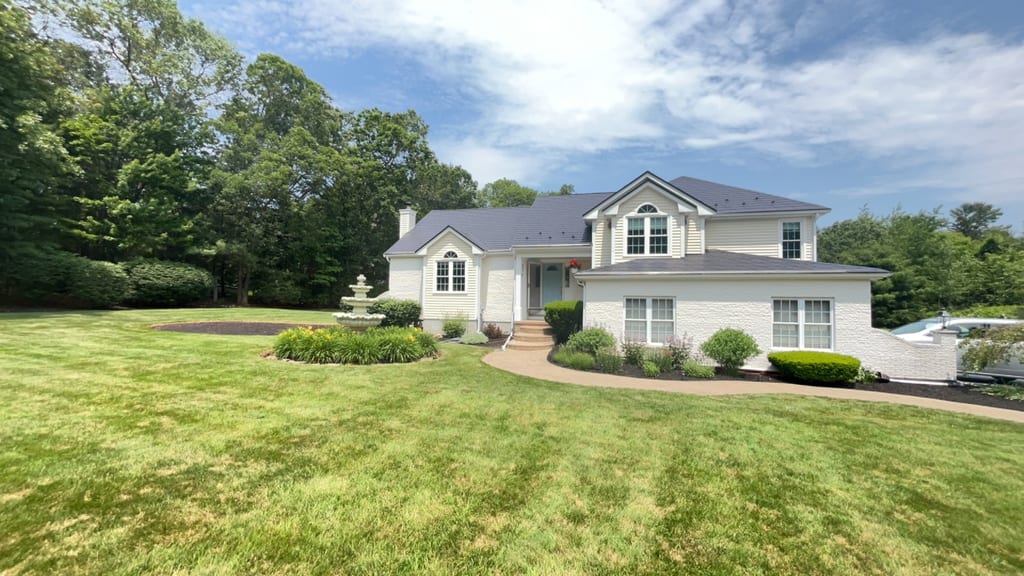 Two-story Colonial home in Wrentham MA with Interlock black aluminum slate metal roof, dormers, chimney, and decorative front fountain.
